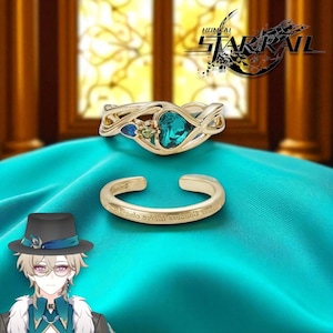 May include: Two gold rings. The top ring has a heart-shaped teal stone and smaller blue and green stones. The bottom ring is a gold cuff with engraved text. The Honkai Star Rail logo is in the top right corner.