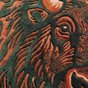 Peut inclure: Gros plan sur un tapis avec un motif de bison. Le tapis pr&eacute;sente un motif d&eacute;taill&eacute; dans des tons de vert et d'orange, avec la t&ecirc;te et les cornes du bison bien en &eacute;vidence. Le motif a un aspect textur&eacute; et sculpt&eacute;.