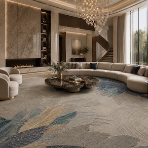 Op de afbeelding: Een luxe woonkamer met een grote, gebogen beige bank, een patroonkleed met blauwe en gouden accenten en een marmeren salontafel. De kamer heeft grote ramen, een open haard en een wenteltrap.