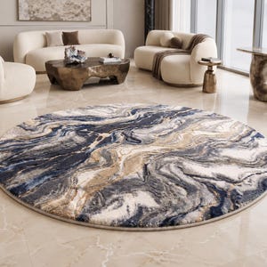 May include: A round area rug with a marbled design. The rug features swirling patterns in shades of blue, gray, beige, and white. The rug is placed on a light-colored tiled floor, and is surrounded by modern furniture.