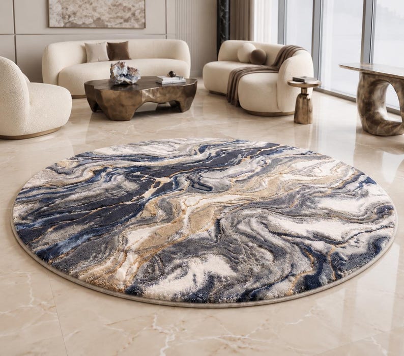 May include: A round area rug with a marbled design. The rug features swirling patterns in shades of blue, gray, beige, and white. The rug is placed on a light-colored tiled floor, and is surrounded by modern furniture.