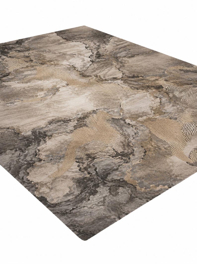May include: A rectangular area rug featuring an abstract pattern in shades of charcoal gray, taupe, and beige. The design incorporates smooth, marbled-like sections contrasted with areas of fine, raised linear textures in a light tan color.