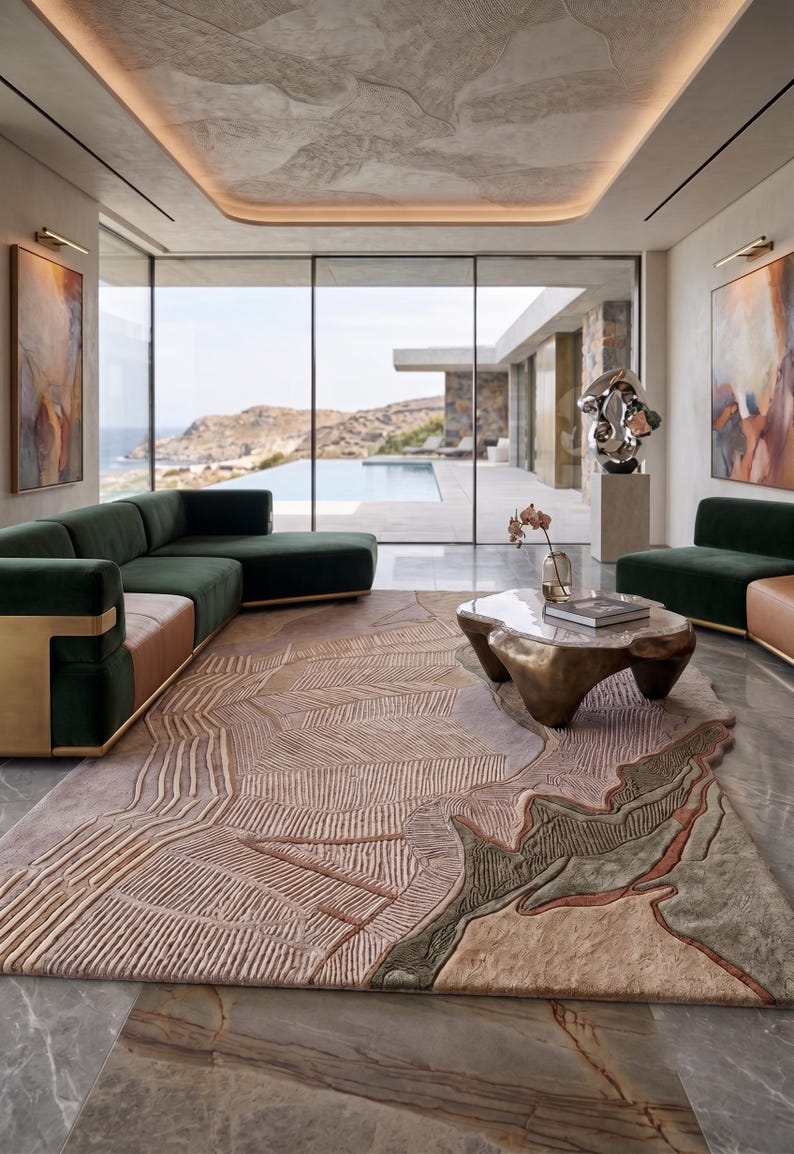 May include: A large rectangular area rug featuring a textured, multi-layered design with abstract topographical patterns in shades of beige, tan, muted green, and soft pink, covering a polished gray marble floor in a spacious living room setting.