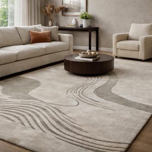 Könnte beinhalten: Ein neutrales Wohnzimmer mit einem großen Teppich mit einem fließenden, abstrakten Design in Grau- und Beigetönen. Der Teppich liegt unter einem beigen Sofa, einem passenden Sessel und einem dunkelbraunen Couchtisch. Eine Lampe und ein Beistelltisch sind ebenfalls zu sehen.