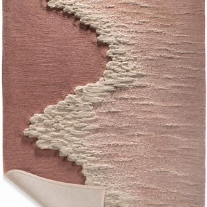 Op de afbeelding: Een rechthoekig, getextureerd tapijt in tinten roze en gebroken wit. Het ontwerp heeft een golfachtig patroon in gebroken wit tegen een roze achtergrond. De rand van het tapijt is licht gekruld en onthult een beige onderkant.