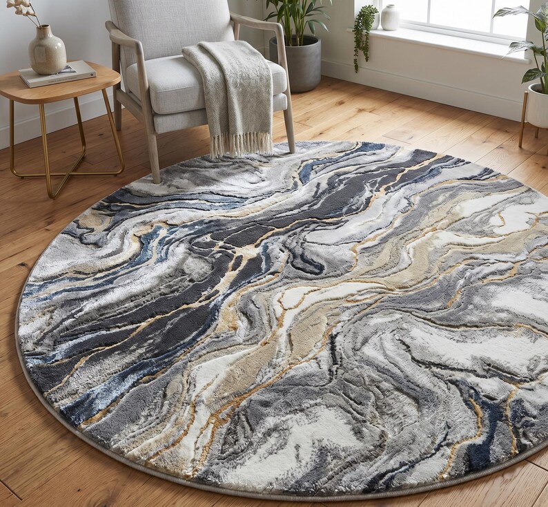 May include: A round area rug with a marbled design in shades of gray, white, and blue, accented with gold lines. The rug is placed on a wooden floor, with a chair and side table in the background. The rug's diameter is approximately 7 feet.