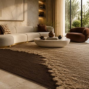 Op de afbeelding: Een moderne woonkamer met een beige hoekbank, een ronde salontafel en een bruine fauteuil. Een groot vloerkleed met een donkerbruin en beige textuurontwerp bedekt de vloer. Een gouden lamp en kunstwerken maken de inrichting compleet.