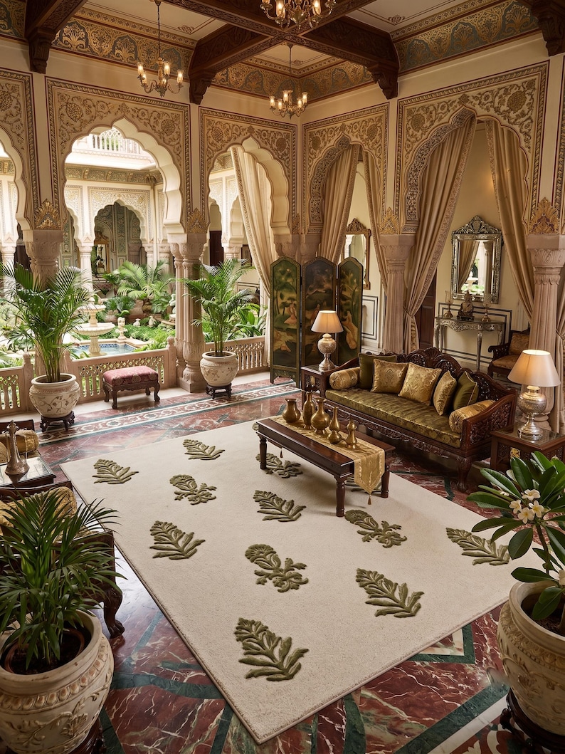 May include: A rectangular area rug featuring a cream-colored base with a repeating pattern of raised, olive-green botanical leaf motifs. The rug is positioned in a room with marble flooring, a wooden sofa, and a wooden coffee table with gold vases.
