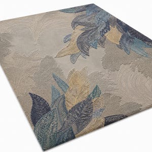 Op de afbeelding: Een rechthoekig vloerkleed met een beige achtergrond en een gedetailleerd bladerontwerp in tinten blauw, goud en groen. De bladeren zijn ingewikkeld patroon, waardoor een textuur ontstaat. Het ontwerp van het vloerkleed voegt een vleugje door de natuur ge&iuml;nspireerde elegantie toe.