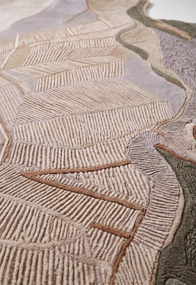 May include: A tufted area rug featuring an abstract landscape design with textured, raised lines in shades of beige, cream, sage green, lavender, and terracotta. The surface displays a mix of high-pile tufted sections and flat-woven areas.
