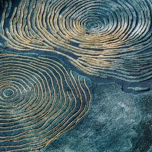 May include: A deep blue area rug featuring a textured, raised pattern of concentric circles in shades of gold and light blue. The surface has a high-low pile construction, creating a tactile, topographical effect with swirling lines across the fabric.