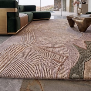 May include: A large area rug featuring a textured, raised linear pattern in shades of dusty pink, beige, and muted olive green. The design consists of geometric shapes and parallel lines that create a tactile, sculpted surface across the entire rug.