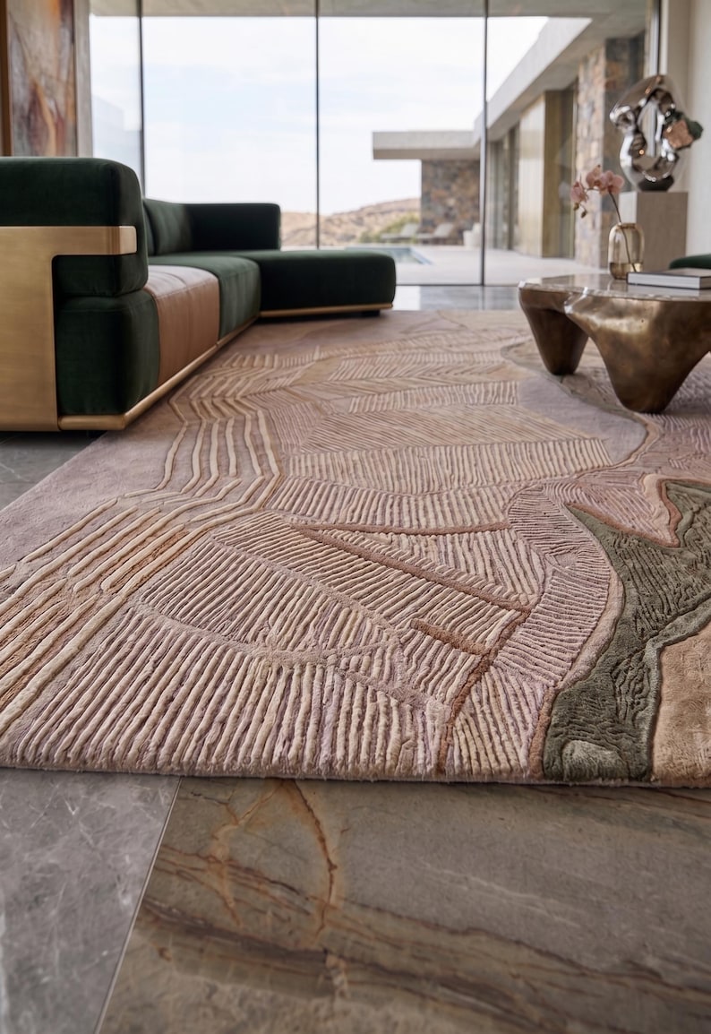 May include: A large area rug featuring a textured, raised linear pattern in shades of dusty pink, beige, and muted olive green. The design consists of geometric shapes and parallel lines that create a tactile, sculpted surface across the entire rug.