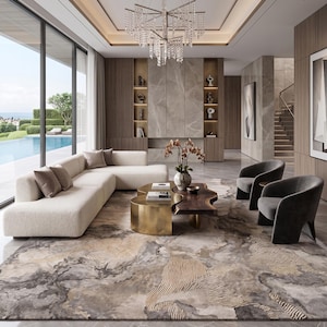 May include: A living room featuring a cream-colored sectional sofa, two dark gray curved armchairs, and a dual-level coffee table with a gold metallic base and a dark wood top. A large area rug with a marbled gray and gold pattern covers the floor.