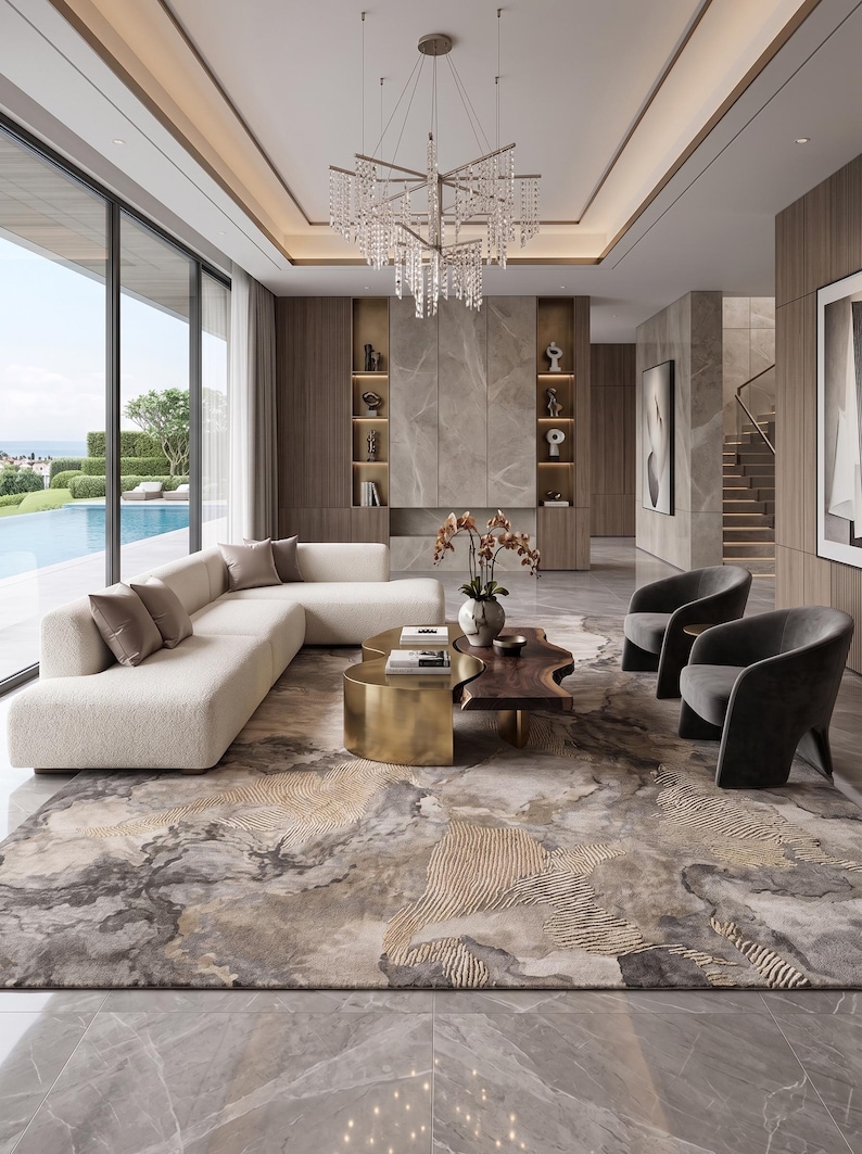 May include: A living room featuring a cream-colored sectional sofa, two dark gray curved armchairs, and a dual-level coffee table with a gold metallic base and a dark wood top. A large area rug with a marbled gray and gold pattern covers the floor.