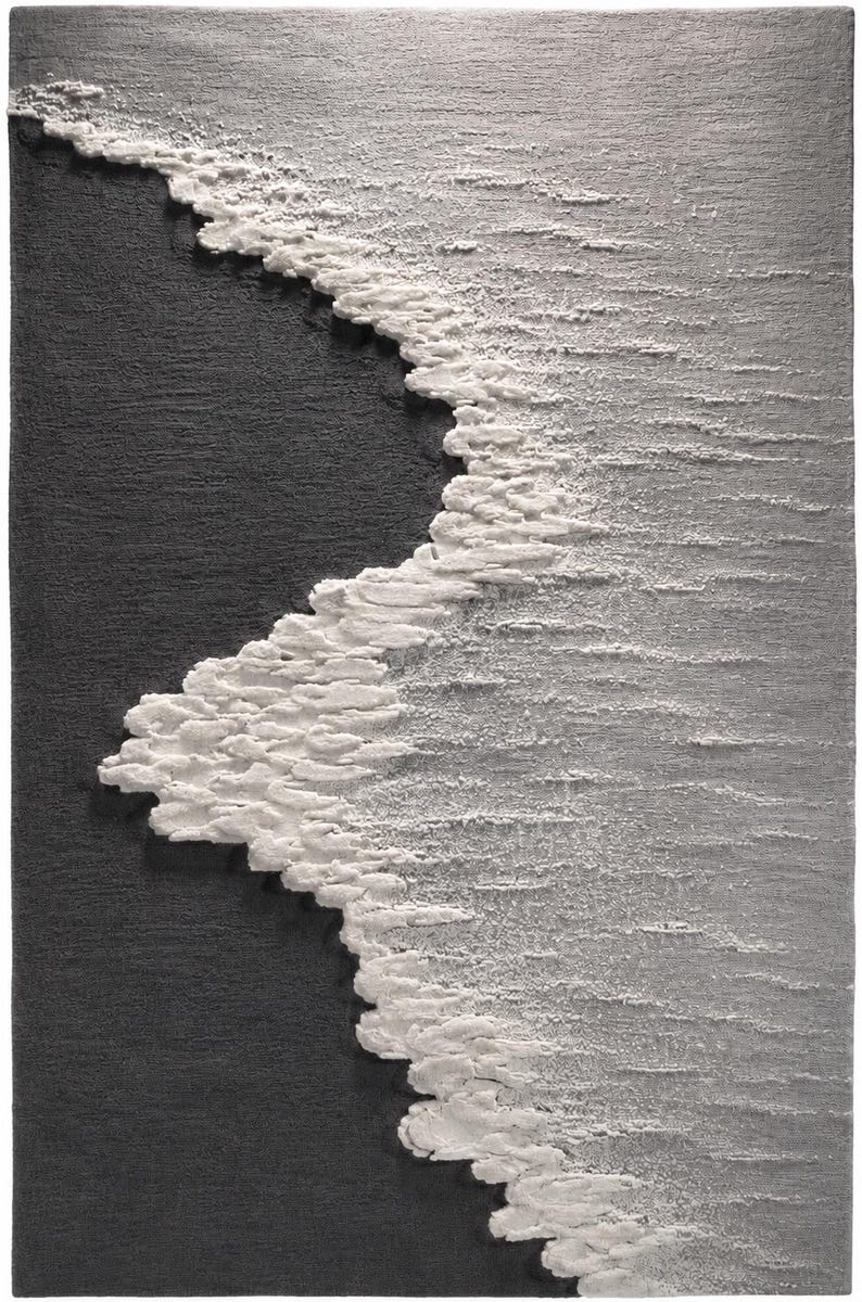 Op de afbeelding: Getextureerde wandkunst met een gestileerde afbeelding van een golf. Het kunstwerk contrasteert een donkergrijs gebied met een witte, schuimige golfkam langs de rand. Het stuk heeft een tastbare, driedimensionale kwaliteit, wat duidt op een reli&euml;fsculptuur.