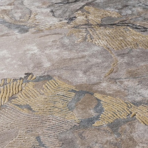 May include: A textured area rug featuring an abstract pattern in shades of beige, taupe, and charcoal gray. The design incorporates raised, carved-style golden-yellow sections with linear detailing that contrast against the smooth, mottled background.