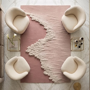 Op de afbeelding: Luchtfoto van een moderne woonkamer. Een blush roze tapijt met een getextureerd golfontwerp wordt omringd door vier cr&egrave;mekleurige, afgeronde fauteuils. De kamer heeft marmeren vloeren en gouden accenten, wat een luxe uitstraling cre&euml;ert.
