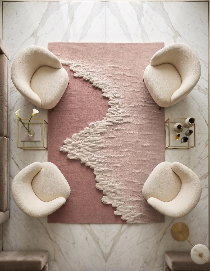 Op de afbeelding: Luchtfoto van een moderne woonkamer. Een blush roze tapijt met een getextureerd golfontwerp wordt omringd door vier cr&egrave;mekleurige, afgeronde fauteuils. De kamer heeft marmeren vloeren en gouden accenten, wat een luxe uitstraling cre&euml;ert.