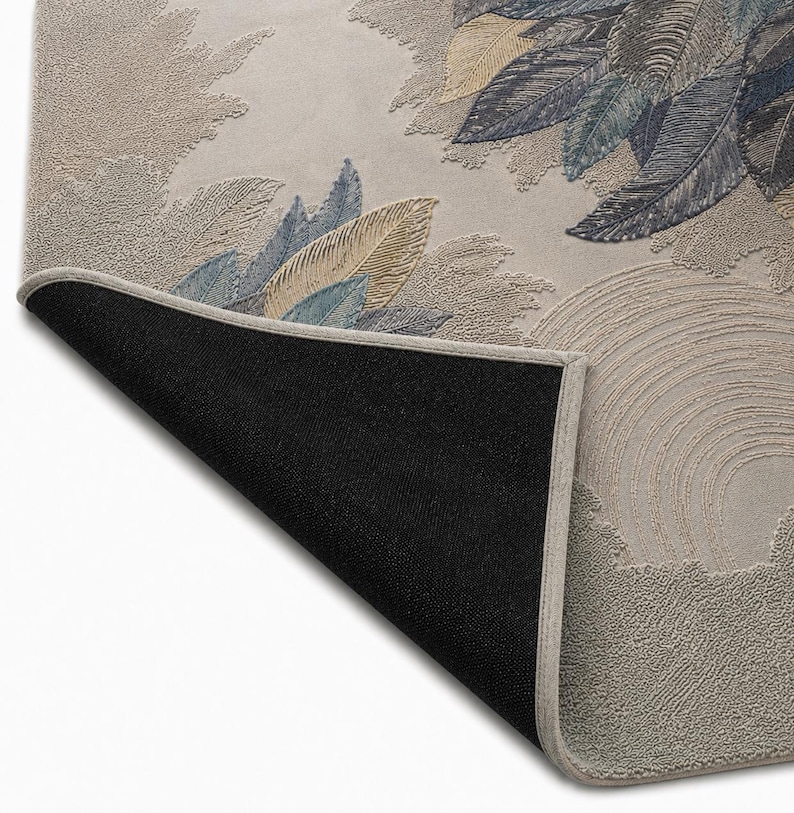 Op de afbeelding: Een rechthoekig tapijt met een gedetailleerd bloemmotief met blauwe, gouden en groene bladeren op een beige achtergrond. De rand van het tapijt is lichtbeige en de onderkant is zwart. Het ontwerp bevat textuurelementen.