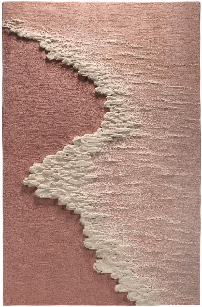 Op de afbeelding: Een getextureerd, abstract tapijt in roze en witte tinten. Het ontwerp heeft een golfachtig patroon in wit, dat contrasteert met de roze achtergrond. Het oppervlak van het tapijt lijkt een verhoogde, driedimensionale textuur te hebben.