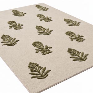 May include: A rectangular area rug featuring a light cream-colored base with a repeating pattern of raised, olive green floral motifs. The design consists of stylized botanical shapes arranged in a grid-like formation across the surface.
