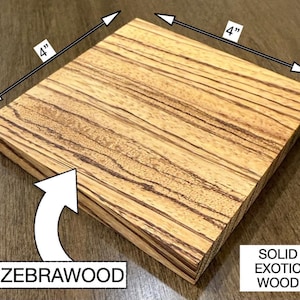 May include: A square block of solid zebrawood, measuring 10 cm on each side, with a distinctive striped pattern. The wood grain is a mix of light and dark brown. The text "ZEBRAWOOD" and "SOLID EXOTIC WOOD" are also visible.
