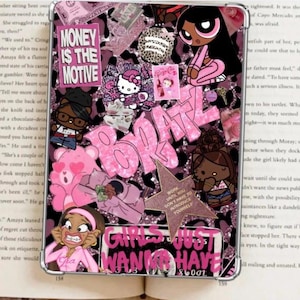 Puede incluir: Una funda decorativa rosa y negra con personajes de dibujos animados, la palabra "BRATZ" y la frase "MONEY IS THE MOTIVE". Otros textos incluyen "GIRLS JUST WANNA HAVE" y "WORK UNTIL YOU DON'T HAVE TO INTRODUCE YOURSELF".