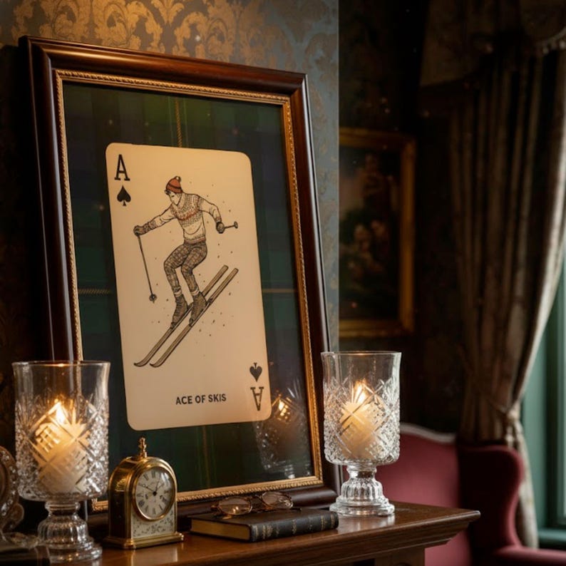 May include: A framed playing card art print featuring a skier on skis, labeled "ACE OF SKIS." The print is displayed on a wooden surface with lit candles in glass holders and a small clock.