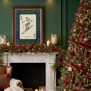 May include: A festive Christmas scene featuring a decorated tree with red ornaments and ribbon. A framed Ace of Skis playing card hangs above a fireplace adorned with garland, candles, and berries. The room has a cozy, holiday atmosphere.