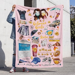 May include: Pink blanket featuring illustrations and text related to the TV show "Gilmore Girls." Includes images of characters, coffee cups, a car, and the text "Gilmore Girls," "Luke's," and "Stars Hollow."