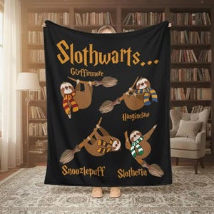 May include: Black blanket featuring the text "Slothwarts..." with illustrations of sloths on broomsticks, each wearing a scarf representing a different house: Gryffinsnore, Hanginclaw, Snoozlepuff, and Slotherin. The blanket is held up in front of a bookshelf.