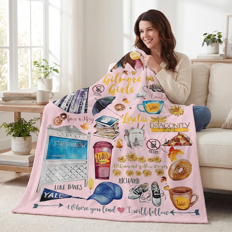 May include: A pink blanket featuring illustrations and text from the TV show "Gilmore Girls." The design includes images of coffee cups, a diner sign, and the text "Where you lead I will follow."
