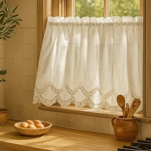Könnte beinhalten: Cremefarbener Küchenvorhang aus Spitze mit gewellten Kanten, der an einem Fenster hängt. Ein kleiner geflochtener Korb mit Eiern und ein Keramiktopf mit Holzlöffeln stehen auf der Holz-Arbeitsplatte. Der Fensterrahmen ist aus Holz.
