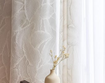 Könnte beinhalten: Weiße Vorhänge mit einem strukturierten Blattmuster. Eine beige Vase enthält getrocknete Blumen und fügt eine natürliche Dekoration hinzu. Die Vorhänge schaffen eine weiche, luftige Atmosphäre, ideal für ein Wohn- oder Schlafzimmer.