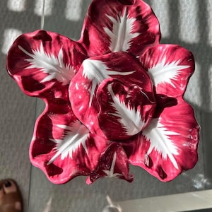 May include: A decorative, flower-shaped serving dish. The dish is a deep red with white accents, resembling a stylized flower. The petals are detailed with white veining. The dish is made of ceramic or porcelain and is likely used for serving food or as a decorative piece.