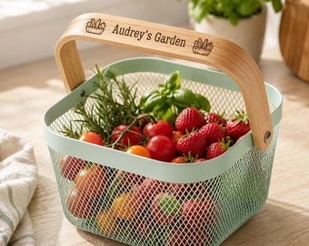 May include: A light green wire mesh basket with a wooden handle engraved with the text "Audrey's Garden" and small plant illustrations. The basket is filled with fresh red cherry tomatoes, green basil leaves, and sprigs of rosemary.