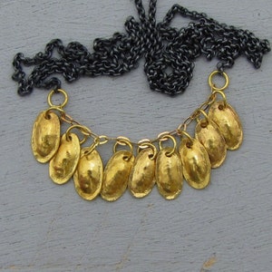 May include: A gold necklace with a black chain and multiple gold oval-shaped pendants. The pendants are attached to the chain with small gold rings.