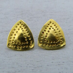 May include: Two gold-coloured stud earrings, triangular in shape. Each earring is covered in small, evenly spaced circular indentations, creating a textured surface. The earrings have a polished finish and a simple, geometric design.
