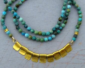 May include: A layered necklace with turquoise beads and a gold pendant with a scalloped edge.