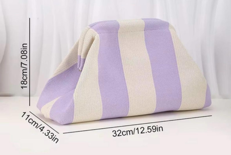 May include: A knit clutch bag featuring vertical stripes in light purple and cream. The bag measures 12.59 inches in length, 4.33 inches in width, and 7.08 inches in height. It has a structured frame opening and a soft, textured fabric construction.