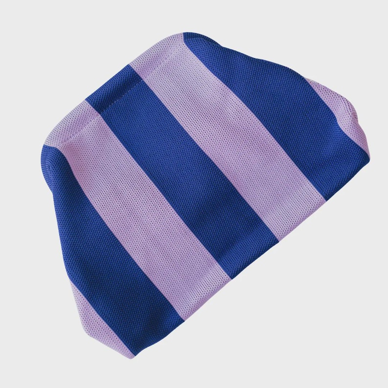 May include: A knit beanie featuring a bold, repeating pattern of wide vertical stripes in alternating shades of royal blue and light lavender. The fabric has a distinct, textured, and uniform knit construction throughout the entire accessory.