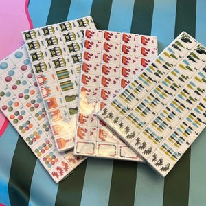 Pu&ograve; includere: Quattro set di tessere Mahjong, ognuno con un design unico. Le tessere sono bianche con simboli e caratteri colorati. I set sono disposti su una superficie a motivi con tonalit&agrave; rosa, verdi e blu.