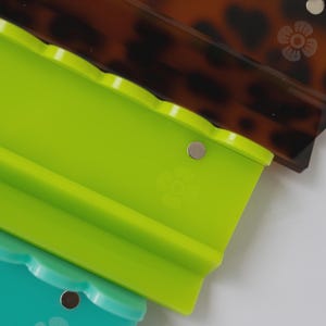 Pode incluir: Tr&ecirc;s organizadores retangulares de pl&aacute;stico com bordas superiores recortadas e um pequeno &iacute;cone de flor gravado na superf&iacute;cie. Cada organizador possui um &iacute;m&atilde; de metal circular embutido perto da borda superior. As cores s&atilde;o casco de tartaruga, verde-lim&atilde;o e azul-petr&oacute;leo.