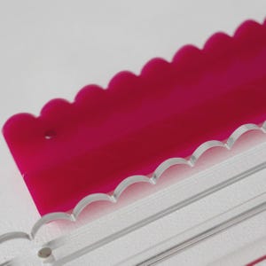 Pode incluir: Uma r&eacute;gua de acr&iacute;lico magenta brilhante com uma borda superior recortada e um pequeno orif&iacute;cio circular perto do lado esquerdo, posicionada parcialmente atr&aacute;s de uma r&eacute;gua de acr&iacute;lico transparente com borda recortada e linhas gravadas.