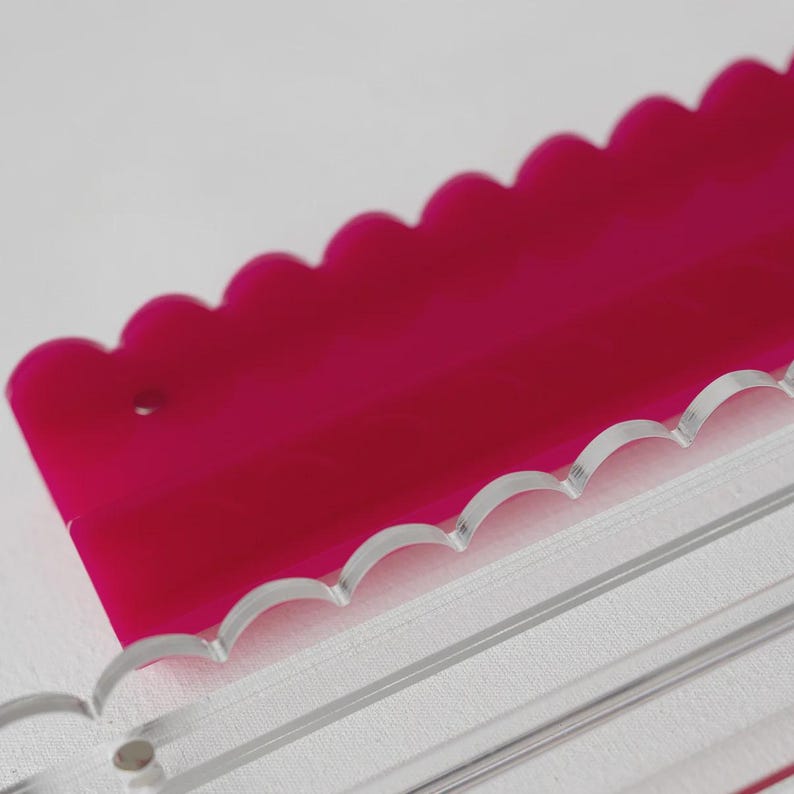 Pode incluir: Uma r&eacute;gua de acr&iacute;lico magenta brilhante com uma borda superior recortada e um pequeno orif&iacute;cio circular perto do lado esquerdo, posicionada parcialmente atr&aacute;s de uma r&eacute;gua de acr&iacute;lico transparente com borda recortada e linhas gravadas.