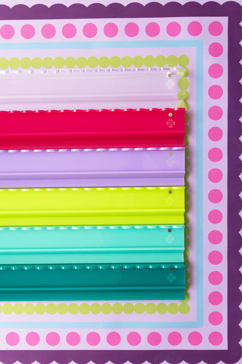 Pode incluir: Um conjunto de seis calhas de exposi&ccedil;&atilde;o retangulares em acr&iacute;lico dispostas verticalmente. As calhas s&atilde;o transparentes, rosa choque, roxo claro, verde lima, turquesa e verde-azulado escuro. Cada calha apresenta um rebordo recortado.