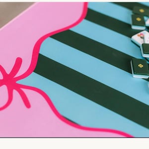 Pu&ograve; includere: Uno schermo di cellulare mostra uno sfondo rosa e blu con la scritta "Mahjong Accessories". L'immagine mostra un gioco di Mahjong in corso con tessere verdi e una superficie a motivi rosa e blu.