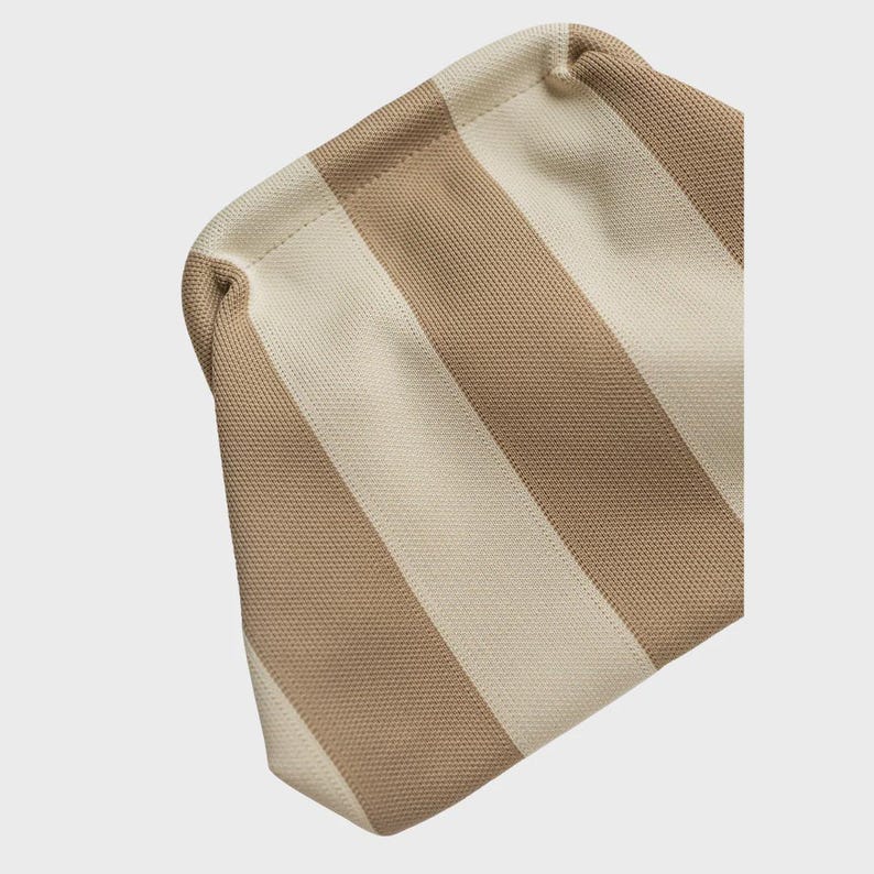 May include: A pouch featuring a knitted texture with alternating vertical stripes in beige and cream. The bag has a rounded top edge and a structured, slightly curved shape, showcasing a consistent woven pattern throughout the entire exterior surface.