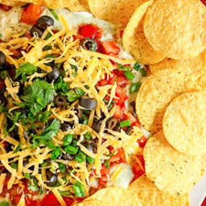 May include: A large bowl of layered dip with tortilla chips on the side. The dip is made with layers of guacamole, salsa, cheese, olives, and cilantro.